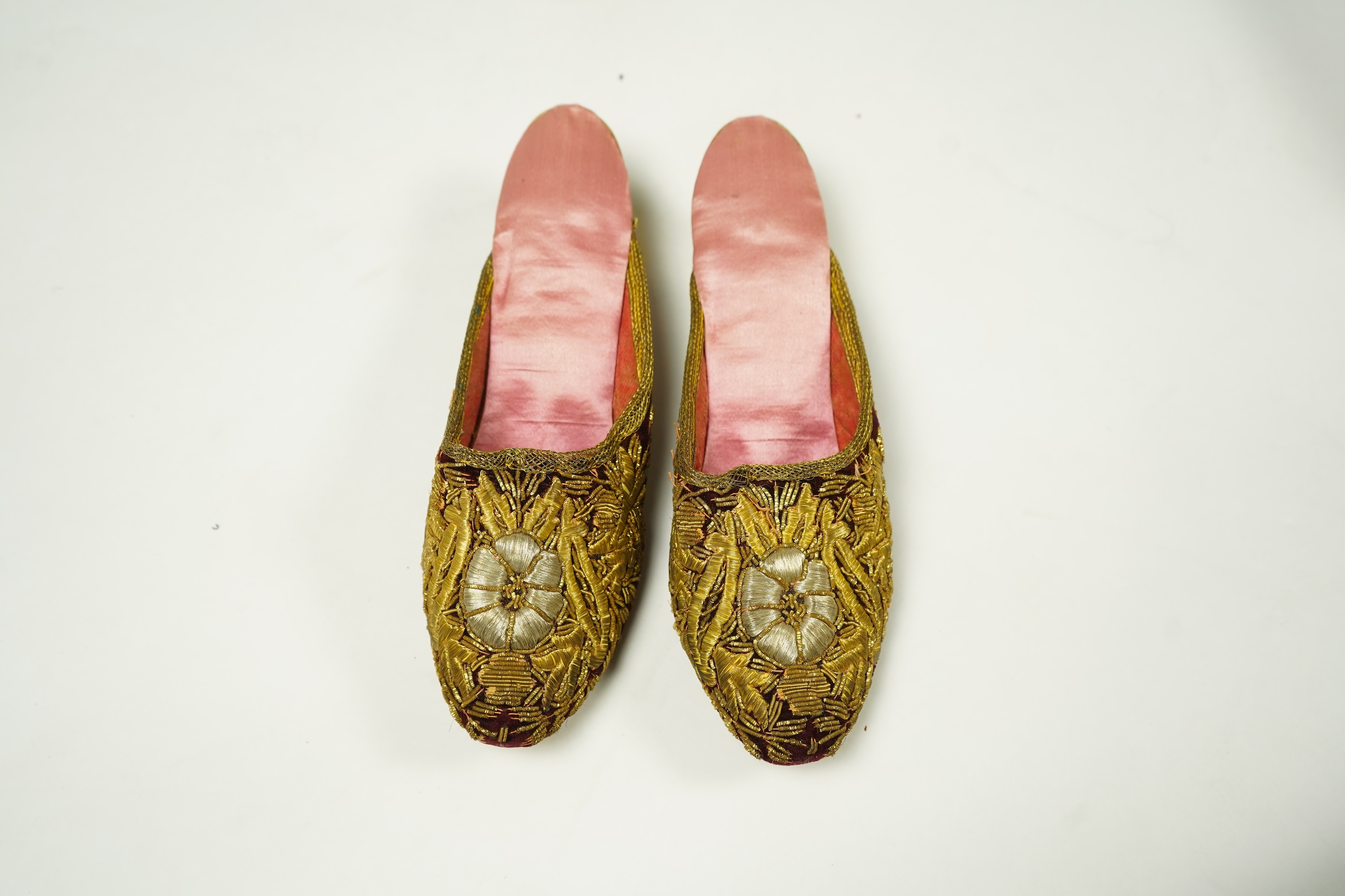 An unusual pair of Edwardian ladies red velvet and gold embroidered mules, a pair of 19th century ladies cream silk shoes and a pair of baby's embroidered suede shoes. Mules stamped 41at toe of sole. Condition - all thre